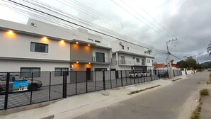 Un edificio residencial moderno con varios pisos, entrada protegida y vista a la calle.