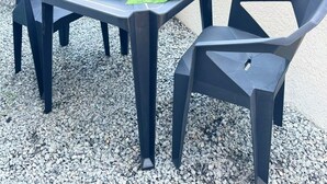 Un patio al aire libre con una mesa preparada para dos personas, rodeada de sillas y una pequeña maceta.