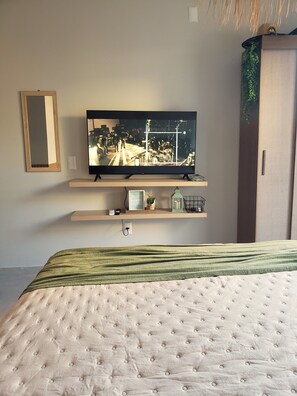 Un dormitorio con cama, televisión en una estantería, espejo y armario.