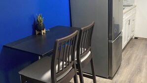 Une cuisine de taille réduite avec un mur d’accent bleu, une table en bois foncé, deux chaises, un réfrigérateur et un four à micro-ondes.