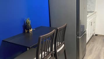 Une cuisine de taille réduite avec un mur d’accent bleu, une table en bois foncé, deux chaises, un réfrigérateur et un four à micro-ondes.