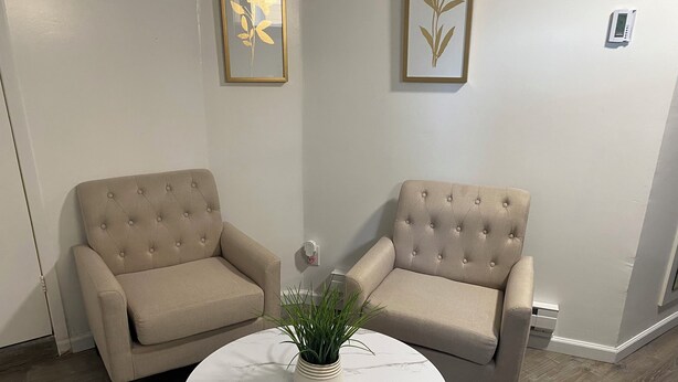 Deux fauteuils beiges à dossier capitonné, une table en marbre blanc sur laquelle est posée une plante en pot, et des œuvres d’art encadrées accrochées au mur.