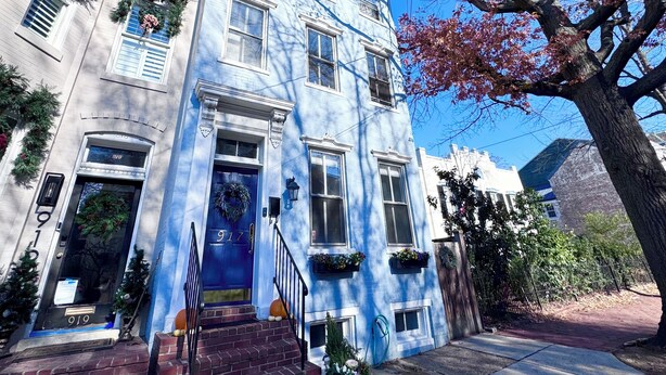 Un edifici blau amb una porta principal, finestres i un arbre al davant.