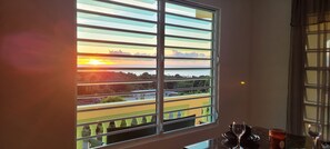 A room with a large window overlooking a scenic view of a sunset over a body of water and greenery. - Private, Cozy 1-bedroom apartment with unobstructed views in serene Patillas (Patillas)