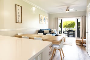 Een moderne eetruimte met een houten tafel en stoelen, een bank met kussens en een plafondventilator.