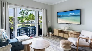 Una sala de estar con televisor, sofá, sillones y un balcón con vista a la playa.