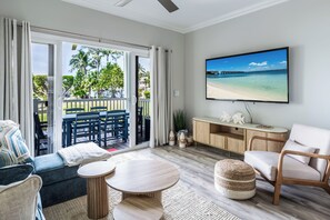 Un salon équipé d’un téléviseur, d’un canapé, de fauteuils et d’un balcon offrant une vue sur la plage.
