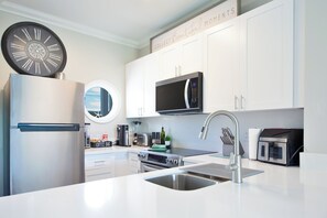 Een moderne keuken met witte kastjes, een ingebouwde magnetron, een roestvrijstalen koelkast en een gootsteen met een moderne kraan.