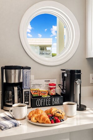 Una mesa de desayuno con barra de café, cafetera, máquina de café, una taza, croissants y un plato de fresas y arándanos.