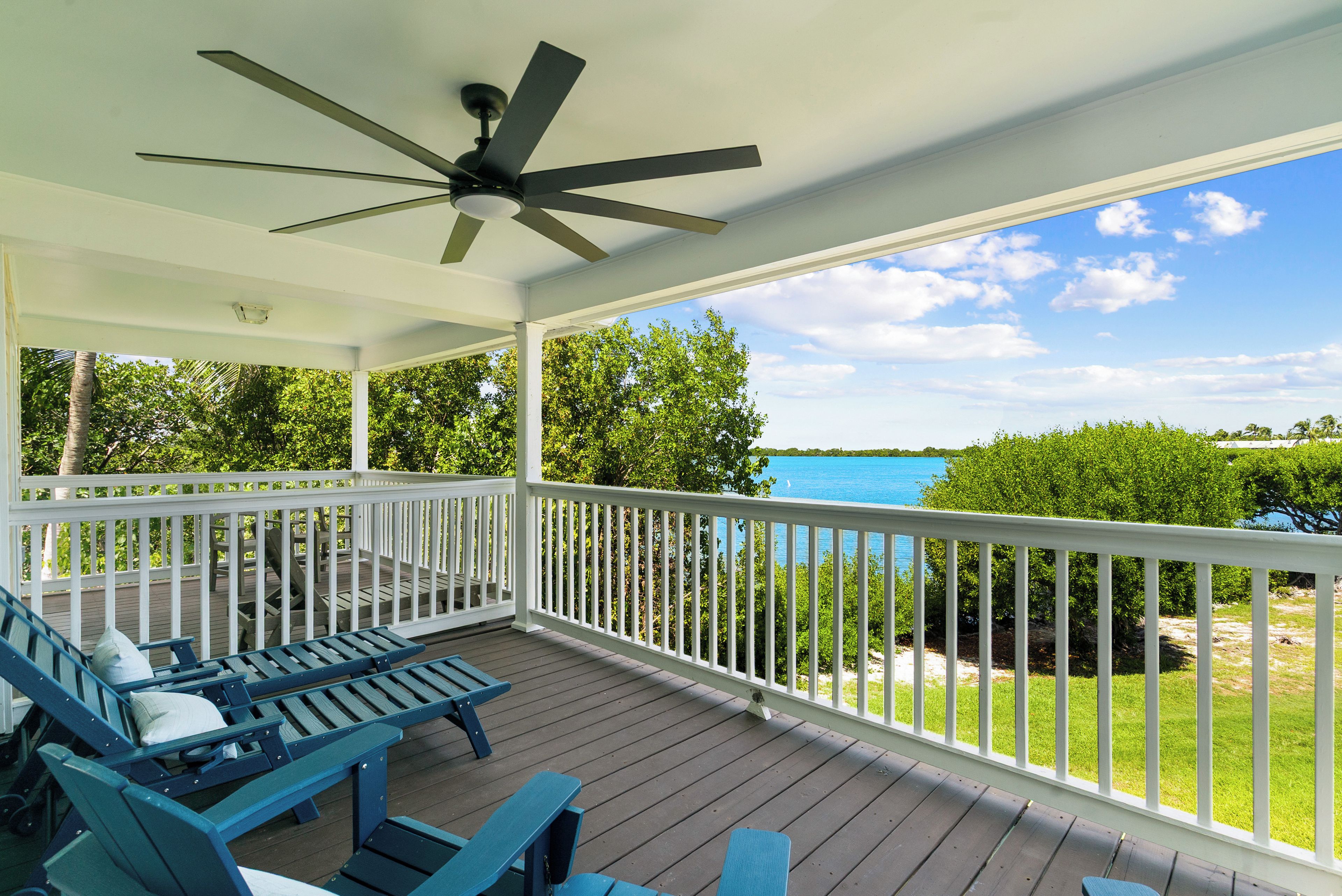 Eine überdachte Terrasse im Freien mit Deckenventilator, weißen Geländern und blauen Bänken.