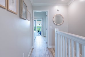 Un couloir orné de tableaux encadrés, un grand miroir rond et une vue sur un balcon extérieur.