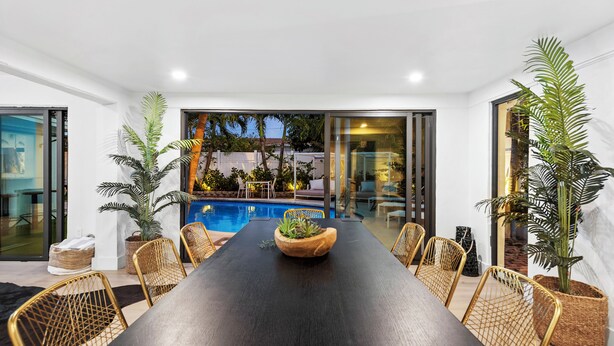 A modern dining area with a long table, wicker chairs, and potted plants. - Villa Azur 8BR Outdoor Oasis with Poolside Bar (Miami)