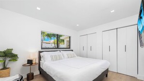 A modern bedroom with a large bed, a bedside table with a lamp, a potted plant, and a wardrobe. - Villa Azur 8BR Outdoor Oasis with Poolside Bar (Miami)