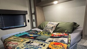 A compact bedroom with a single bed, a window with blinds, and a small bedside table.
