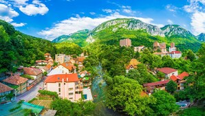 Une ville de montagne dont les bâtiments sont entourés d’une végétation luxuriante et bordée par une rivière.