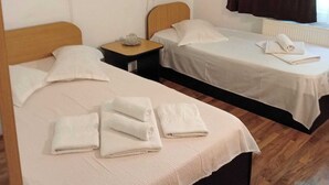 Une chambre d’hôtel avec deux lits simples, une tête de lit en bois, une petite table de chevet, un radiateur et une fenêtre avec des rideaux.