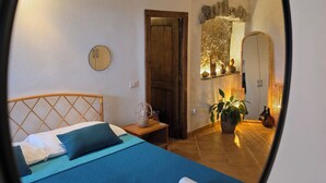 Ein Schlafzimmer mit einem Bett, einem Nachttisch, einem Spiegel, einer Tür und einer kleinen Topfpflanze.