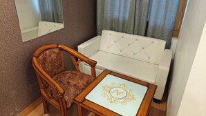 A small room with a wooden chair, a white sofa, a small table with a decorative item, and a mirror on the wall. - Hotel advantage inn  (Prayagraj)