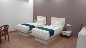 A hotel room with two beds, a chair, a bedside table, and a wall socket. - Hotel advantage inn  (Prayagraj)