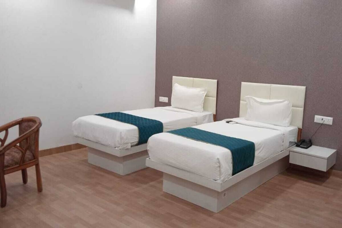 A hotel room with two beds, a chair, a bedside table, and a wall socket.