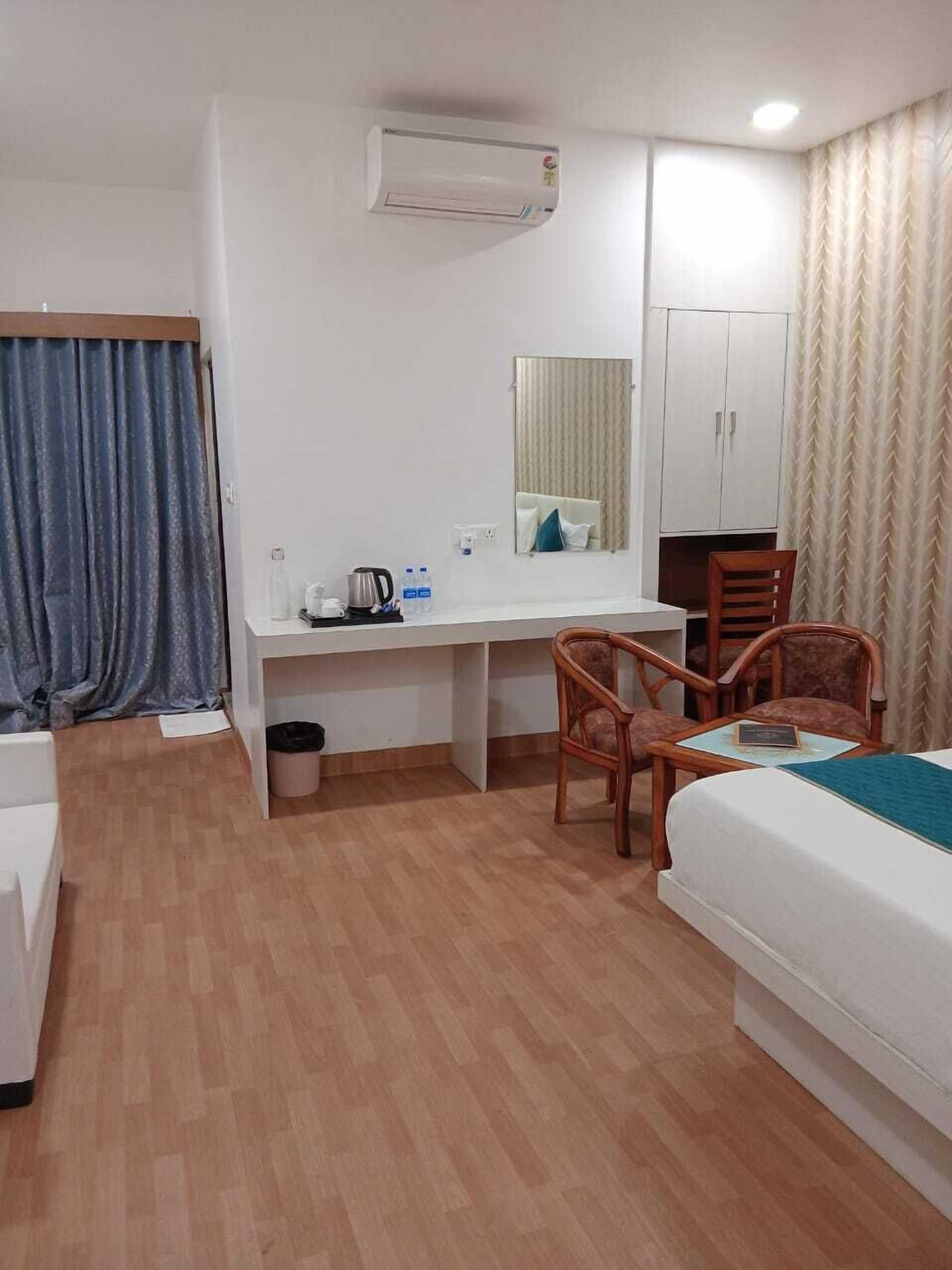 A hotel room with a bed, desk, chairs, a mirror, an air conditioning unit, and a wardrobe.
