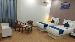 A hotel room with two beds, a desk, two chairs, a lamp, and a painting on the wall. - Hotel advantage inn  (Prayagraj)