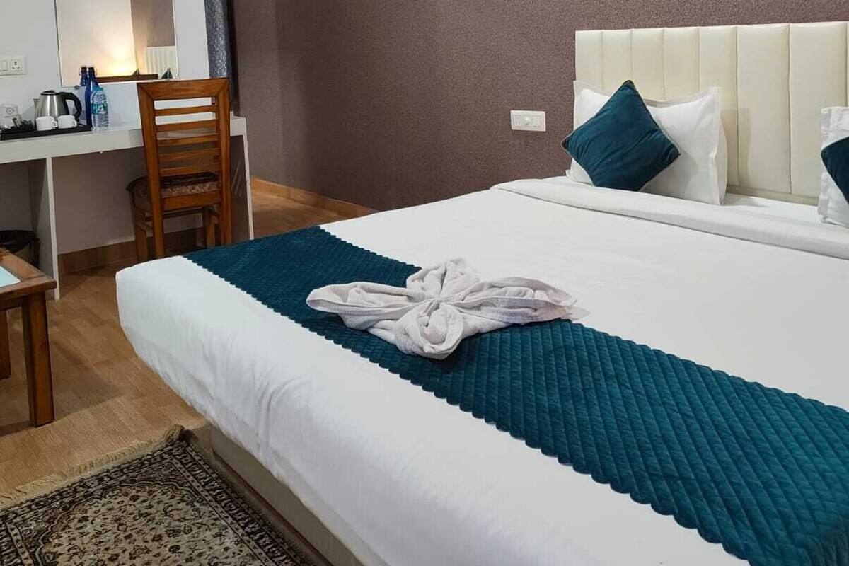 A hotel room with a bed, a desk, a chair, a mirror, and a painting on the wall.