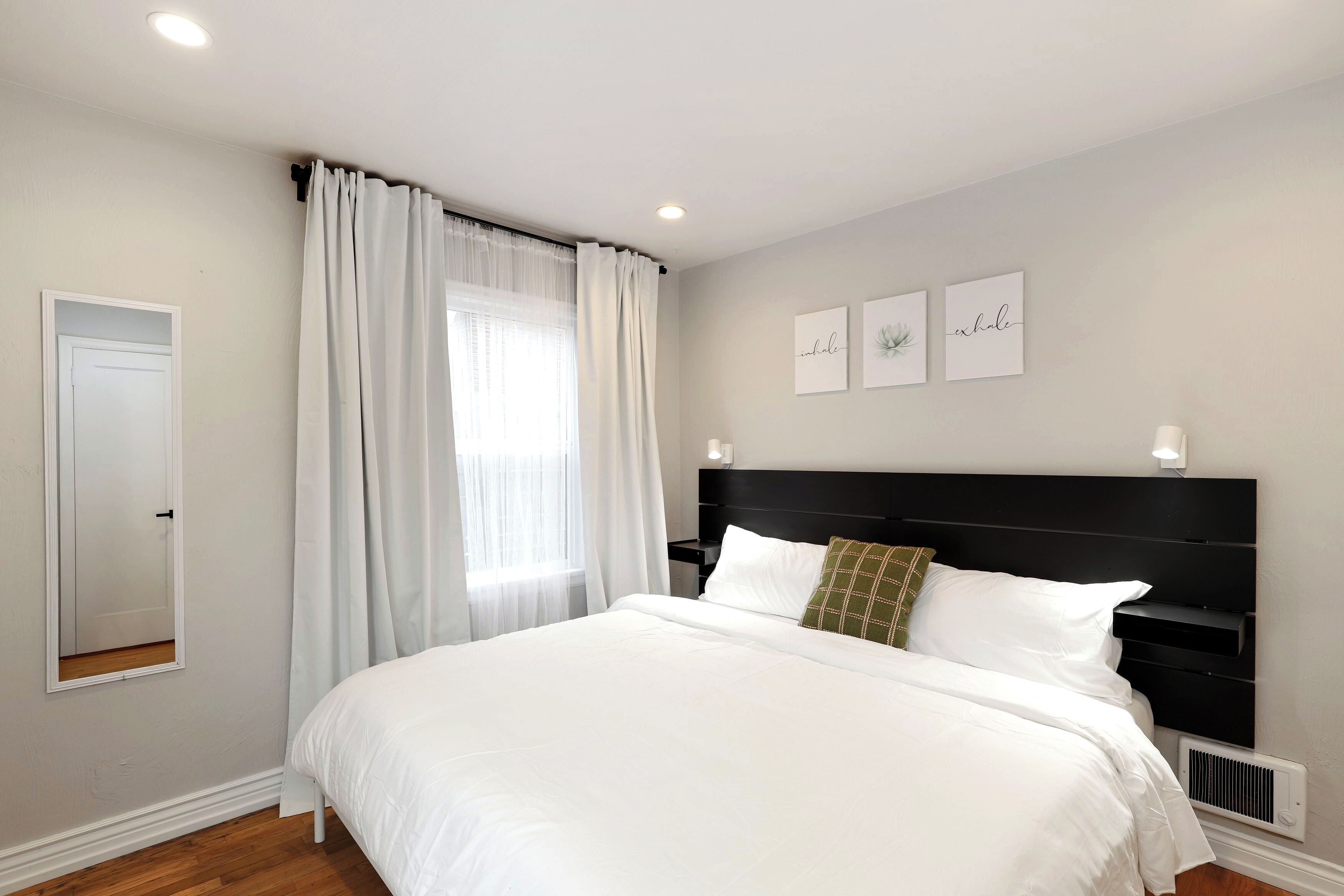 A bedroom with a large bed, a bedside table, a mirror, and a window with curtains.
