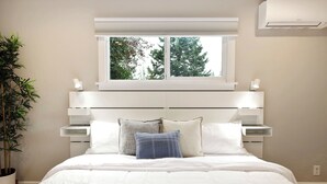 Een slaapkamer met een bed, een wit hoofdbord, nachtkastjes, een raam en een kamerplant.