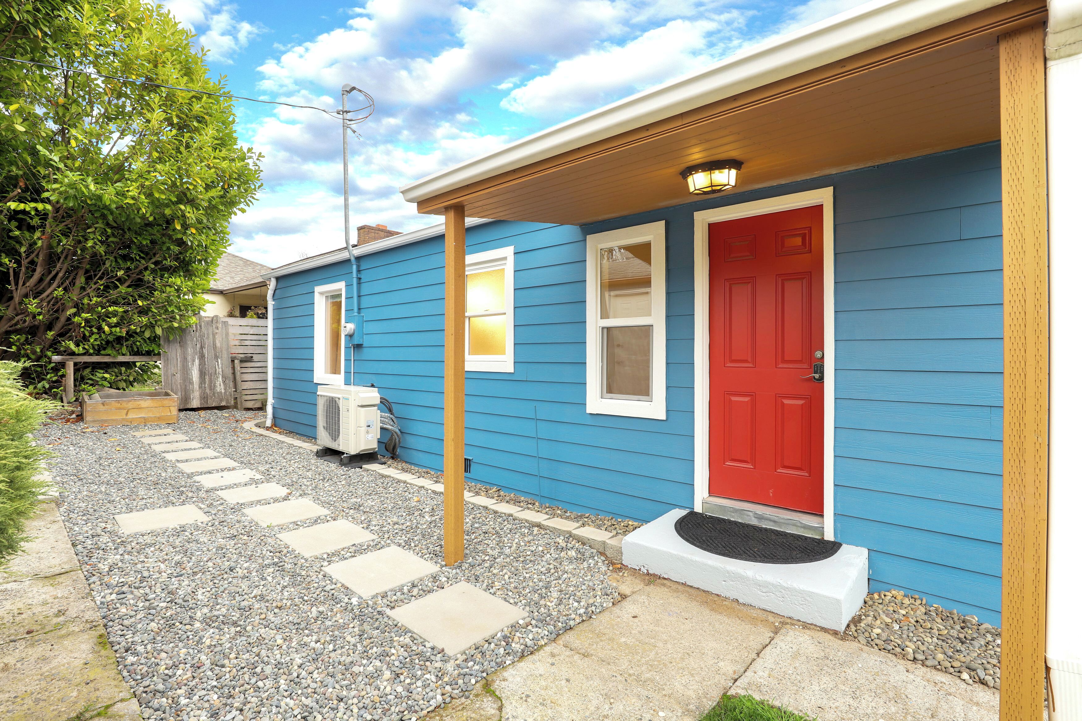 A blue house with a red door, a covered porch, and a gravel pathway.
