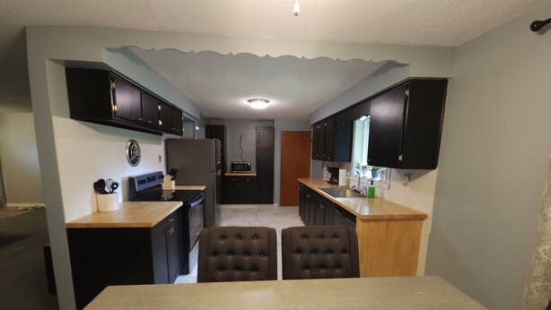 A compact kitchen with dark cabinets, a central island with seating, and a microwave. - Relaxing Ranch (sodus)