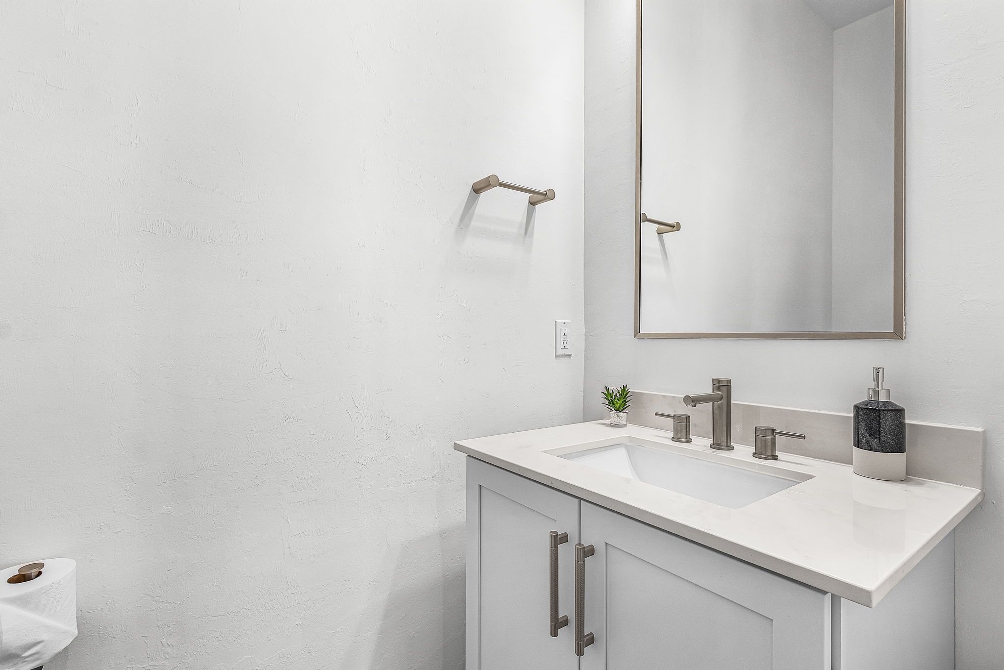 Un baño moderno con un lavamanos blanco, un espejo y un perchero para toallas.