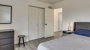 Quarto com cama, penteadeira, um banquinho pequeno e guarda-roupa com portas deslizantes.