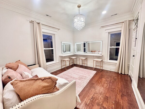 A bedroom with a large bed, a vanity with mirrors, and a chandelier.