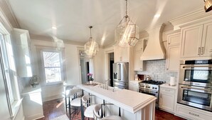 A modern kitchen with white cabinetry, a central island with bar stools, stainless steel appliances, and pendant lighting.