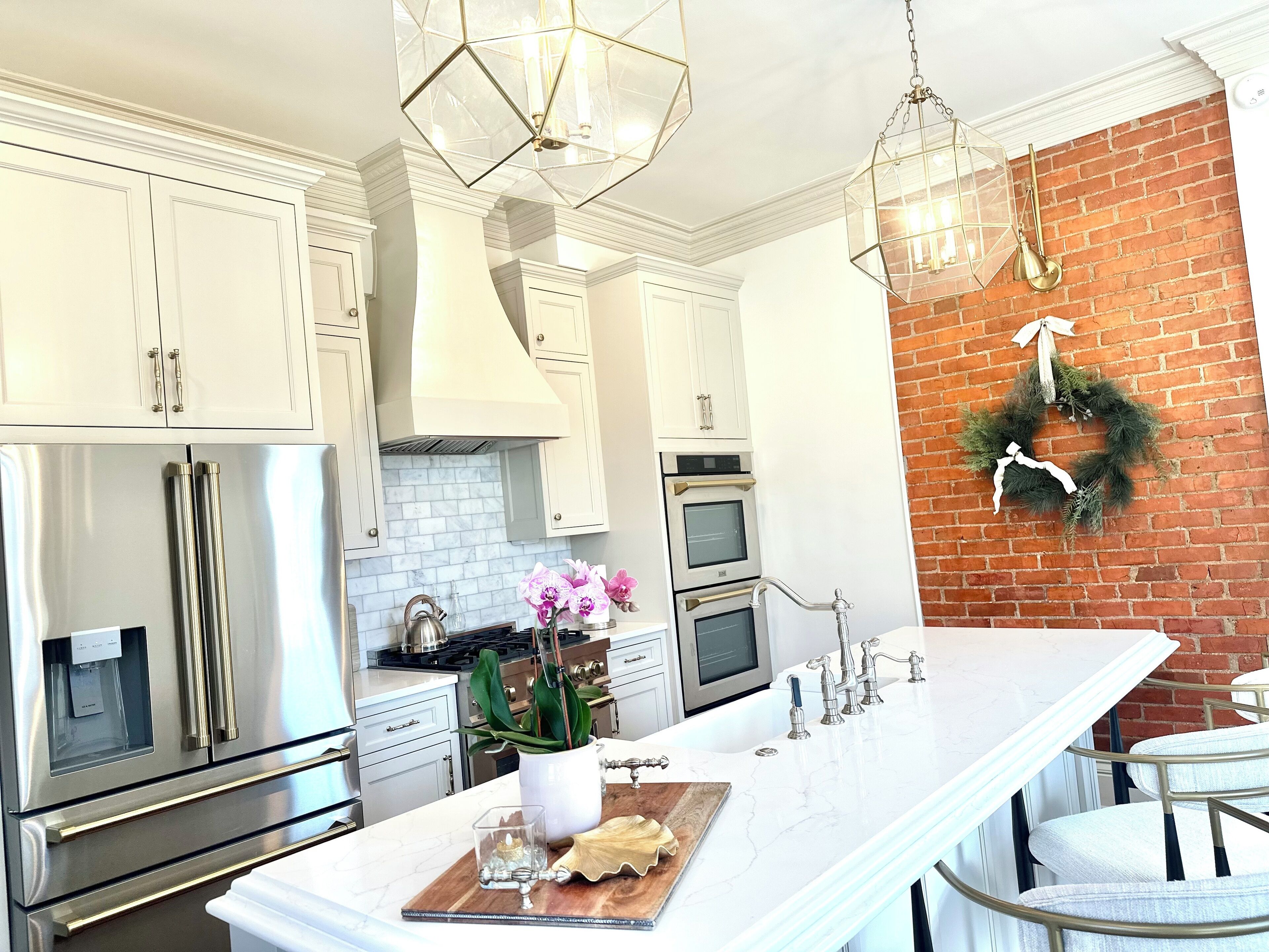 Een moderne keuken met witte kastjes, roestvrijstalen apparatuur, een marmeren aanrechtblad en een accentmuur van baksteen.