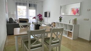 Una sala de estar moderna con un sofá gris, sillas blancas, una mesa de comedor de madera y un televisor montado en la pared.