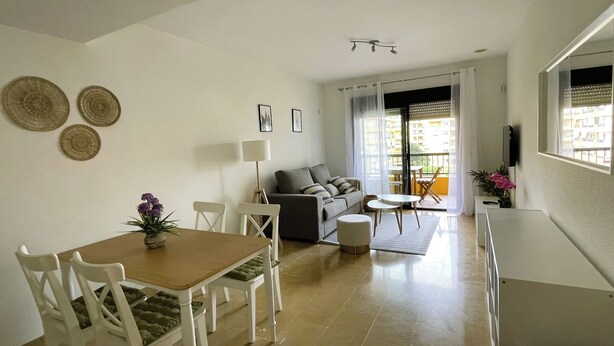 Una sala de estar moderna con un sofá, una mesa de comedor y sillas. Cuenta con un balcón con vistas a edificios.