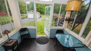 Une véranda avec une table et des chaises en verre, une lampe et une vue sur une maison et un jardin.