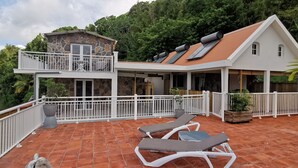 Ein zweistöckiges Haus mit Balkon, einer überdachten Terrasse mit Liegestühlen und einer steinernen Fassade.