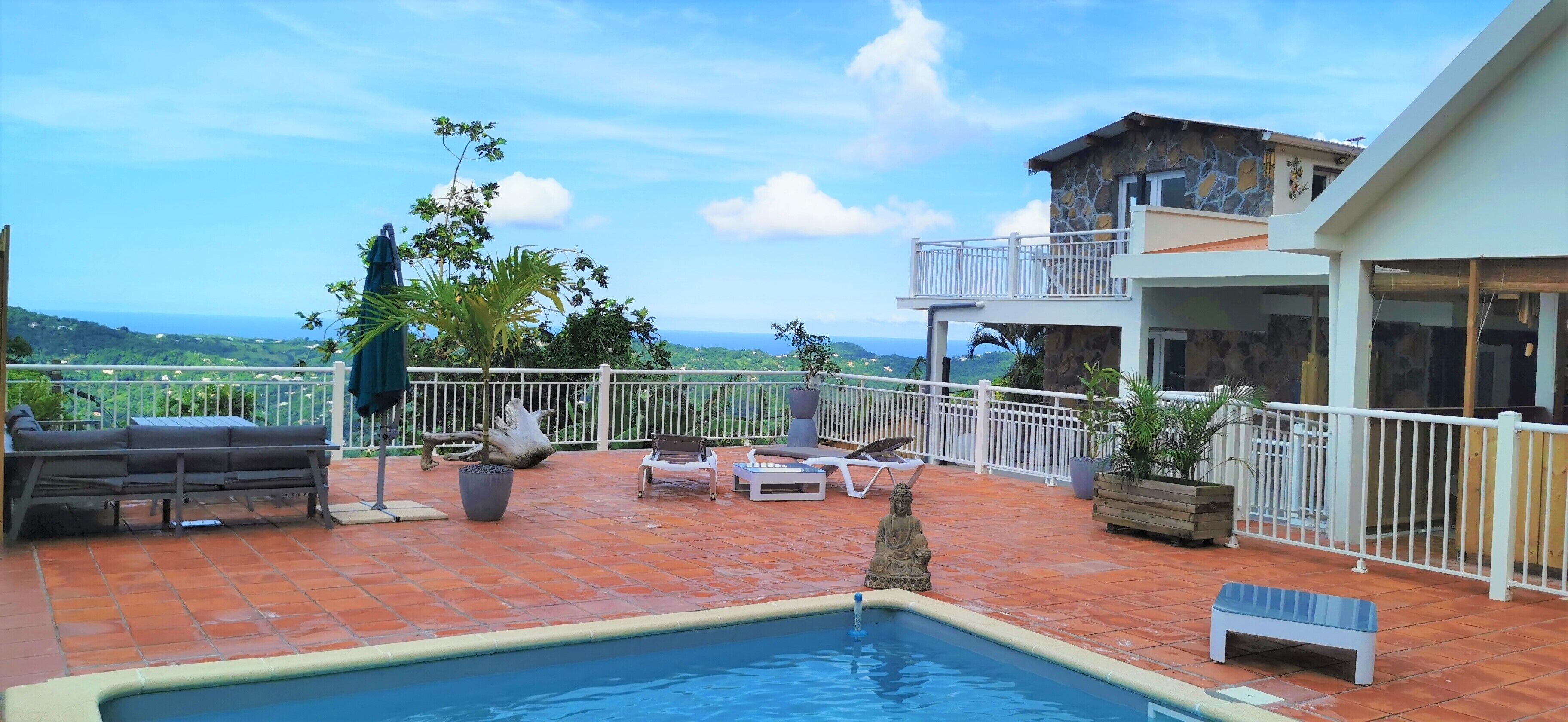 A rooftop pool area with a view of the ocean, outdoor seating, and a statue.