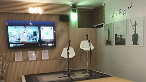 Ett modernt rum med en stor tv-skärm, ett piano och inramade musikinstrument på väggen.