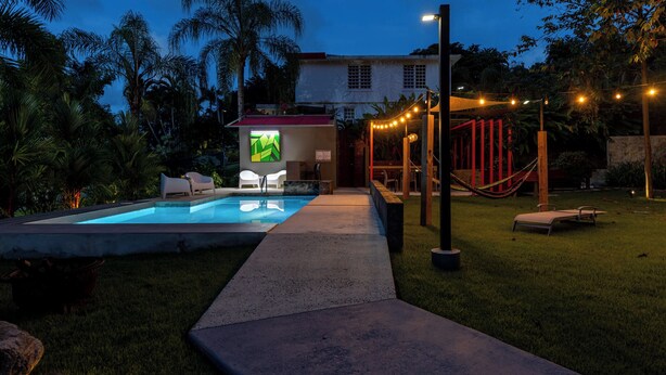 Une piscine avec une terrasse en béton, un hamac et des guirlandes lumineuses.