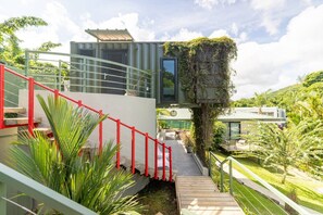Un edificio moderno con una escalera, barandilla roja y vegetación.