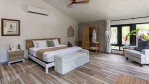 A modern bedroom with a bed, bedside tables, a wardrobe, a seating area, and a view of greenery through the windows. - Mata e’ Plátano Guesthouse Suite private pool (Mata de Platano)