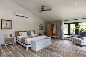 Un dormitorio moderno con cama, mesitas de noche, armario, zona de estar y vistas a zonas verdes por las ventanas.