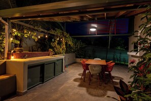 Un patio exterior con una mesa y sillas de madera, un lavadero empotrado y plantas en macetas.