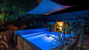 A hot tub with a blue-lit interior, surrounded by plants and a wooden deck. - Mata e’ Plátano Guesthouse Suite private pool (Mata de Platano)