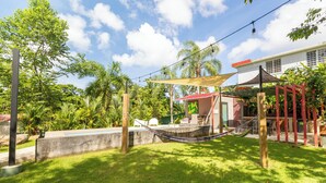 Un hamac dans un jardin luxuriant, avec une terrasse, une piscine et une maison en arrière-plan.