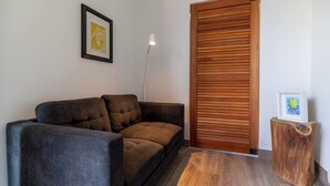 Un salon moderne avec un canapé marron foncé, un plancher en bois, un tableau encadré au mur et une table d’appoint en bois.